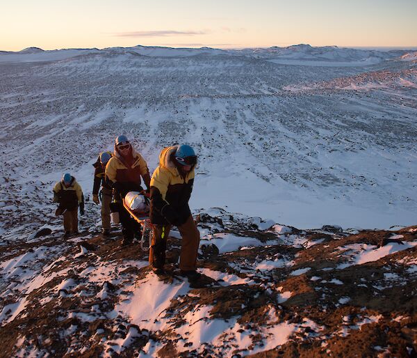 A group of people walking a stretcher up a hill