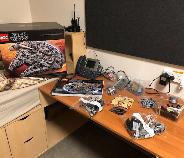 The contents of a Lego box laid out on a desk with the empty box behind showing the Milennium Falcon