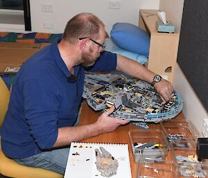 A man sitting at a desk constructing a large lego model