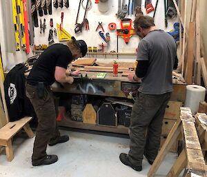 Two mean working at workbench, once using a file.  Various tools are displayed on a board above.