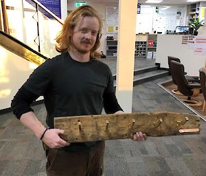 A man smiling to camera holding a home made wooden coat rack