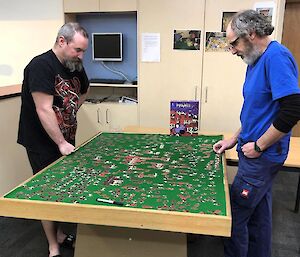 Two men standing at a table covered in green cloth, completing a jigsaw