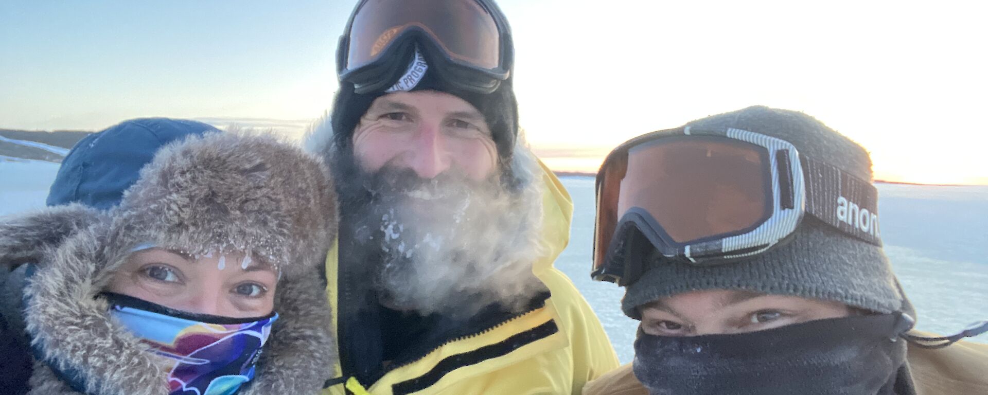 A selfie of three expeditioners, in hats and scarves, feeling happy that they completed the job