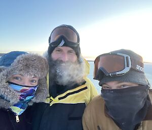 A selfie of three expeditioners, in hats and scarves, feeling happy that they completed the job