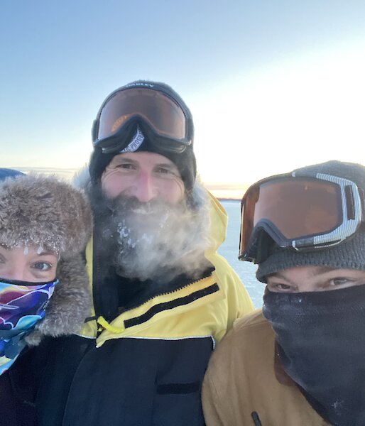 A selfie of three expeditioners, in hats and scarves, feeling happy that they completed the job