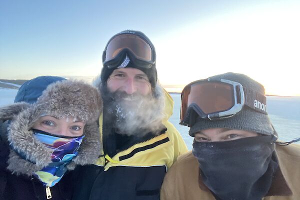 A selfie of three expeditioners, in hats and scarves, feeling happy that they completed the job