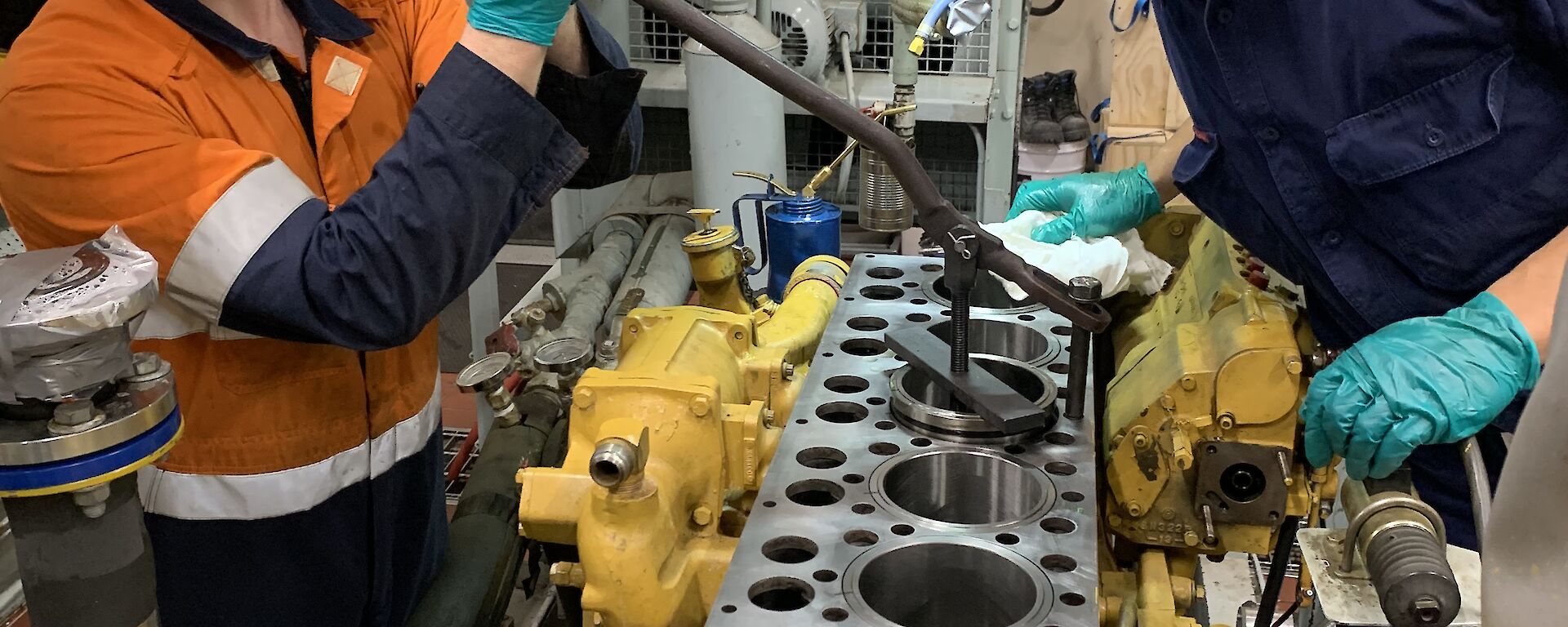 2 men in a workshop repairing the inside of a generator engine.  One is smiling to camera, the other examining the parts.