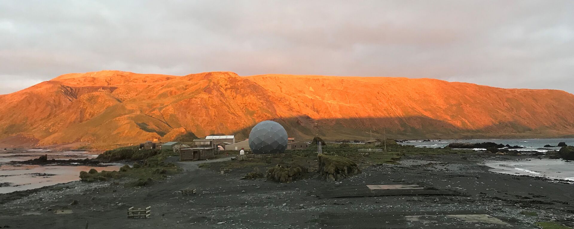 A view of the buildings on station.  The mountain behind has been lit orange by the sunset.