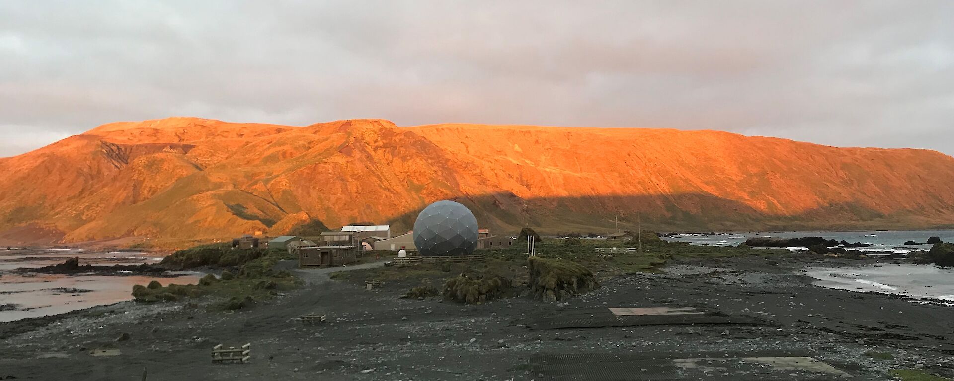 A view of the buildings on station.  The mountain behind has been lit orange by the sunset.