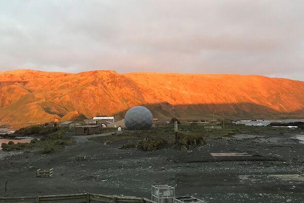 A view of the buildings on station. The mountain behind has been lit orange by the sunset.