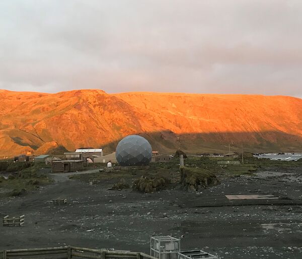A view of the buildings on station. The mountain behind has been lit orange by the sunset.
