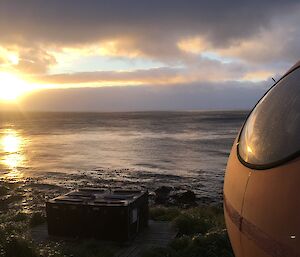 A view across the sea towards the setting sun.  The side of a small orange 'pod' hut can be seen to the right of the image.