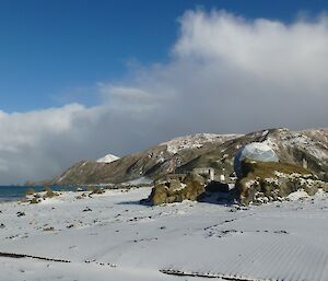 A sandy beach with a small group of buildings behind and snow capped mountains at the rear