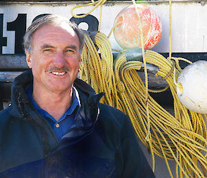 A man standing beside some ropes and buoys attached to a boat.