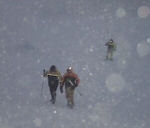 3 people in the blizzard snow marking a path to hut with canes