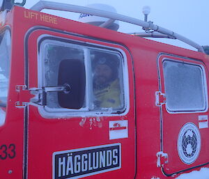 Looking in the window of a red Hagglunds vehicle.  A man sits in the drivers seat smiling.