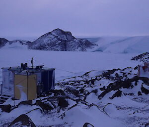 Looking across a snowy plateau.  A small yellow hut is visible in the foreground.