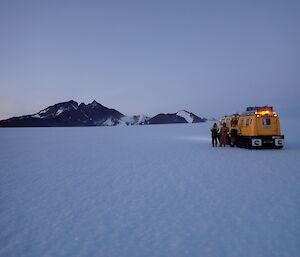 The yellow Hagglund over snow vehicle parked on the plateau with Mt Henderson rising out of the ice cap in the background.