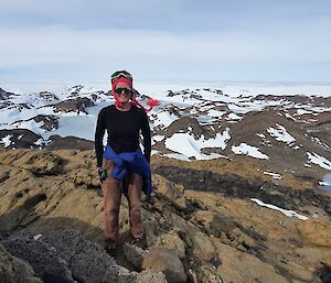 Woman standing on rocky outcrop with snow covered hills in the background