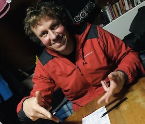 A man sitting at a table, smiling to camera and pointing to his Yhatzee score sheet