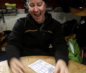 A lady laughing, looking at 5 dice on the table in front of her, all showing sixes
