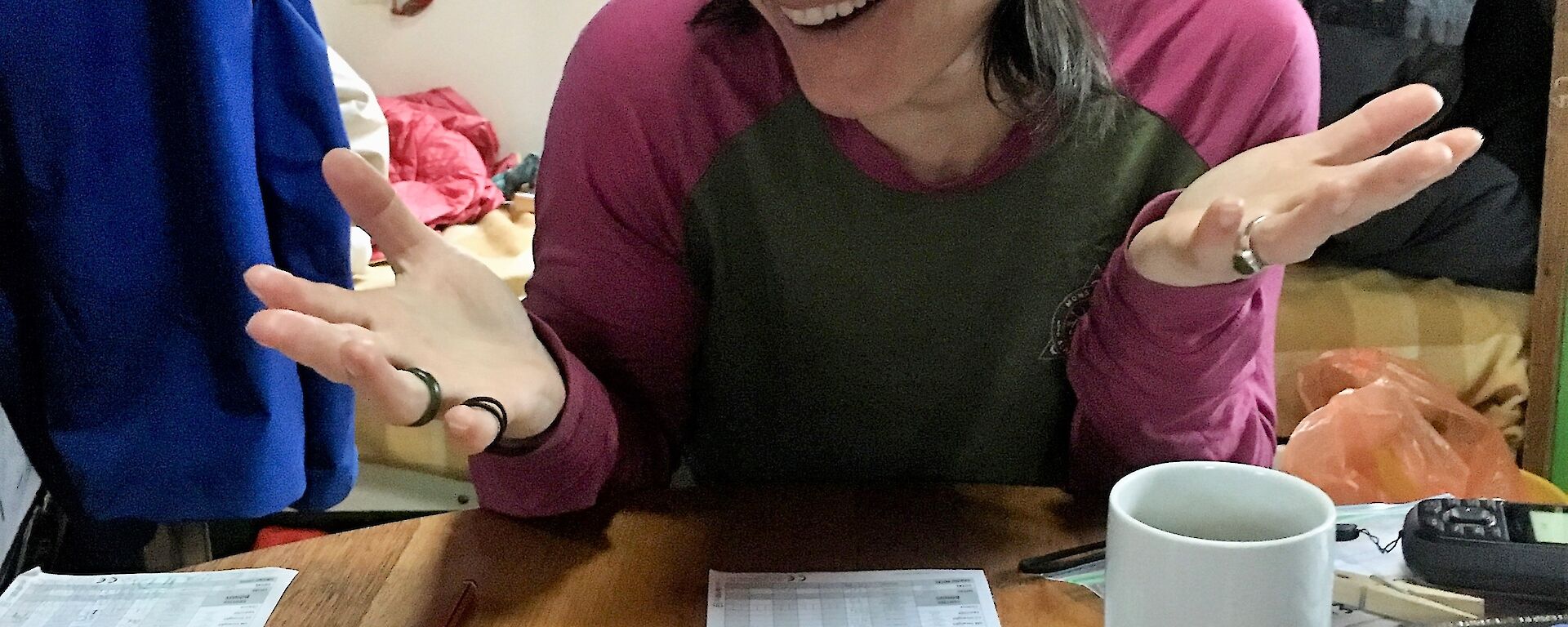 A women shrugs and smiles at camera, with five dice all showing three on the table in front of her