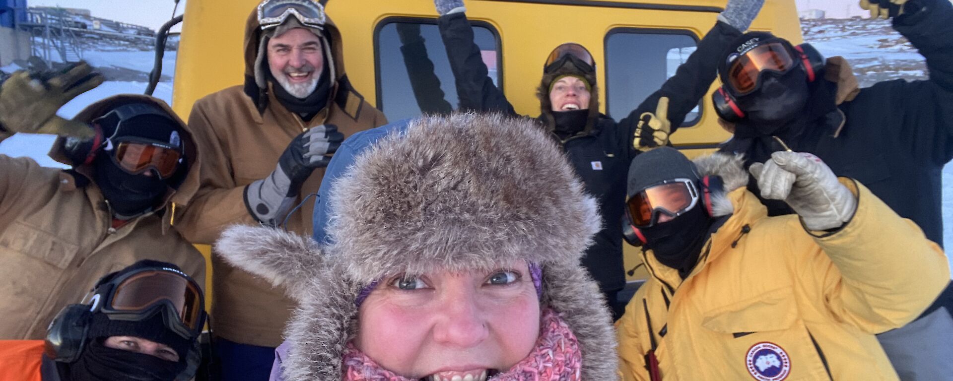 Selfie photo of excited expeditioners standing in front of the yellow Hagglund vehicle.