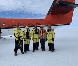 Group of five people in front of an aircraft on snow runway.