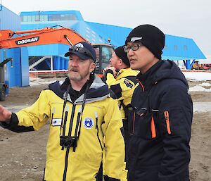 Man in yellow speaks with man in black in front of blue building.