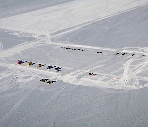 Aerial image of runway groomed in snow with buildings and vehicles arranged in rows alongside.