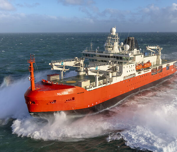 A large red ship powering through a rough ocean.