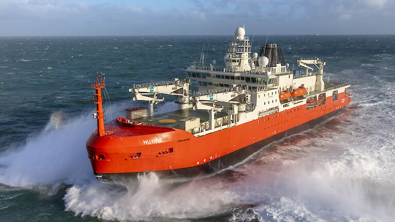 A large red ship powering through a rough ocean.