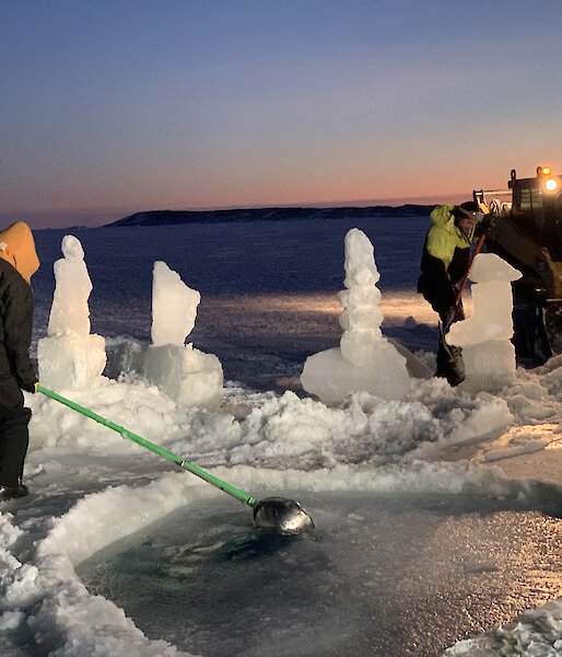 A man is scooping reformed ice out of an ice hole pool with ice sculptures around it.