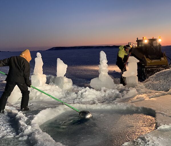 A man is scooping reformed ice out of an ice hole pool with ice sculptures around it.