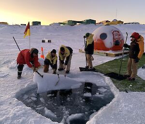 A crew hauling a large chunk of ice out of an ice hole as others look on