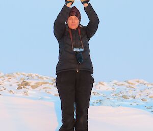 A female standing in the snow holding her hands above her head to look as if she is 'holding' the moon