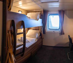 One of the ship's cabins with a bunk bed and desk either side of a port hole.