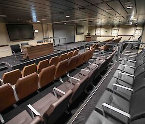 Rows of padded seats looking towards a large screen TV and desk on a raised level.