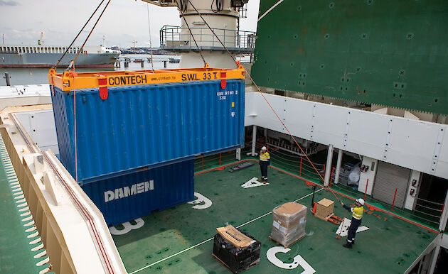 A shipping container being craned into place on the ship's foredeck.