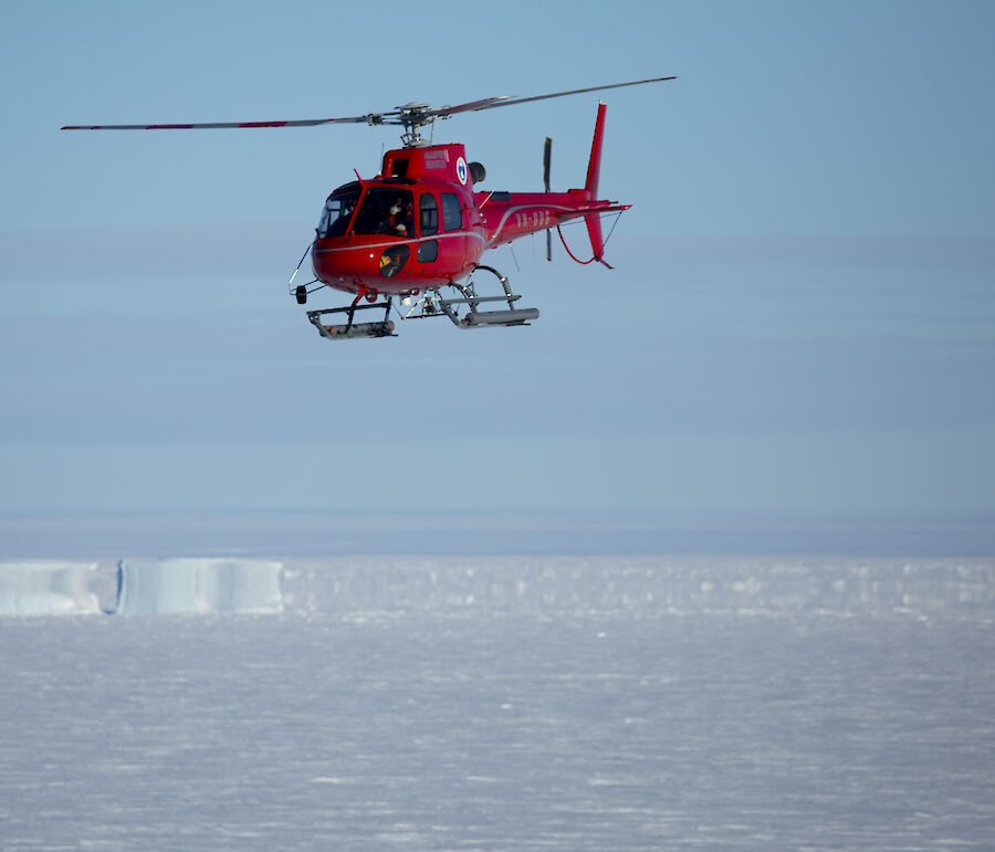 A red helicopter flying above sea ice.