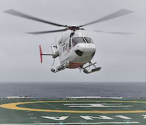 white helicopter lands on green heli deck