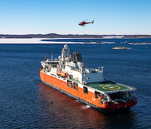 A red icebreaker in a blue sea with a red helicopter above