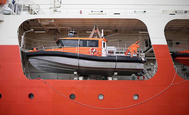 Small orange boat stowed on larger ship.