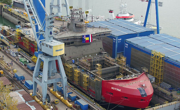 Nuyina under construction in the dry dock surrounded by cranes, warehouses and containers.