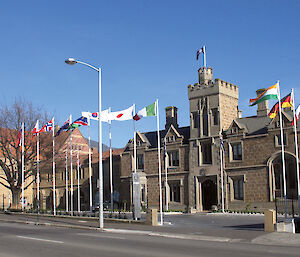 A sandstone building with flags of different countries flying outside.
