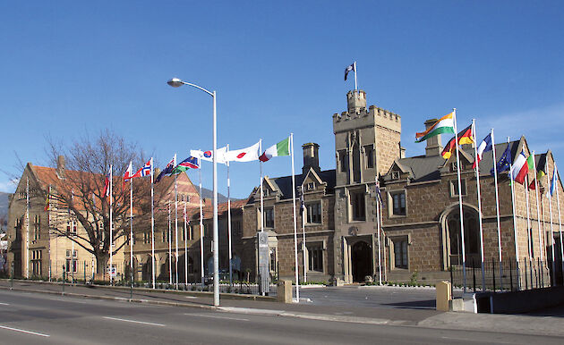 A sandstone building with flags of different countries flying outside.