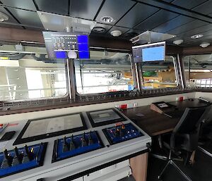 Inside of a room with control panels, desk, chairs and display screens, with large windows overlooking the science deck.