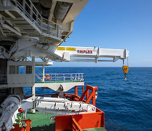 Machinery on the green deck of a ship. A large white crane is attached to the roof of the space.