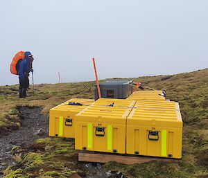 A man with a backpack standing next to the yellow boxes that make up the cache