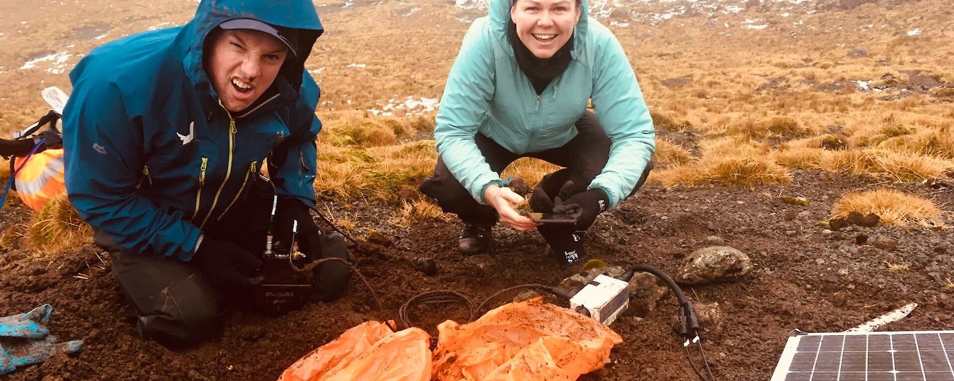 Two expeditioners squatting next to a solar panel in the field